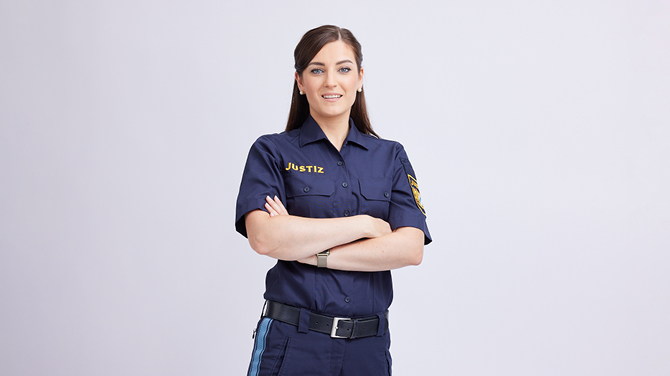 Justizwachtmeisterin Isabelle A. in Uniform. Sie lächelt freundlich und verschränkt die Arme.